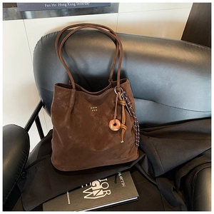 Close-up of vintage brown suede tote bag with delicate gold logo and side charm