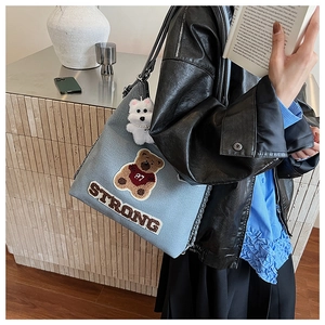 Dettaglio della borsa tote in denim blu con ricamo a orsetto, catena e ciondolo peluche