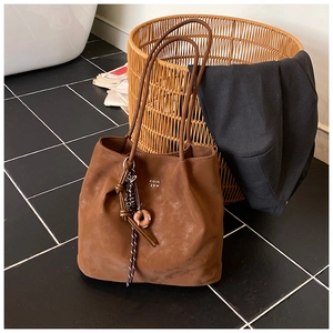 Detail view of brown suede tote bag with slim shoulder straps and woven knot charm