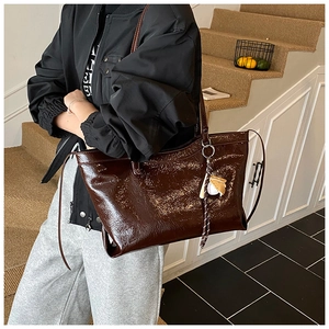 Détail d'un sac cabas marron foncé brillant avec bandoulière et pendentif sur un mannequin