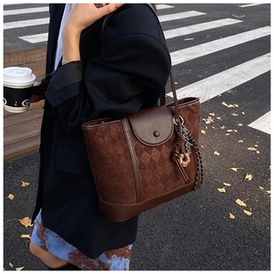 Detail of dark brown tote bag with quilted suede texture and stylish decorative pendant