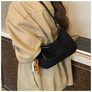 Dettaglio borsa sottobraccio in camoscio nero con ciondolo in legno e finiture dorate