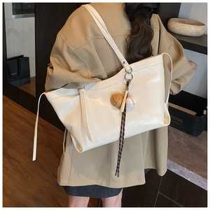 Détail d'un grand sac cabas blanc cassé en cuir verni brillant avec pendentif de baseball