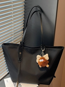 Grand sac cabas noir minimaliste avec pendentif monstre en peluche dans un décor