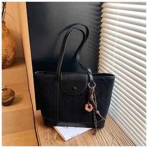 Close-up of black quilted tote bag with matte finish and donut charm detail