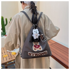 Dettaglio zaino grigio con toppa a forma di orsetto e ciondolo a cane su outfit casual chic