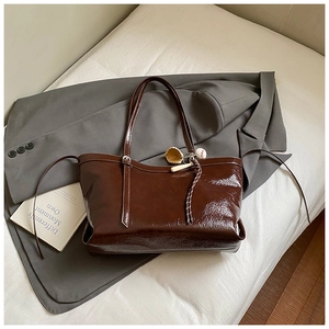 Détail du grand sac cabas marron brillant avec breloque de baseball sur veste grise