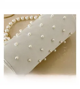 Detailed close-up of white cylindrical handbag with pearl embellishments and beaded handle