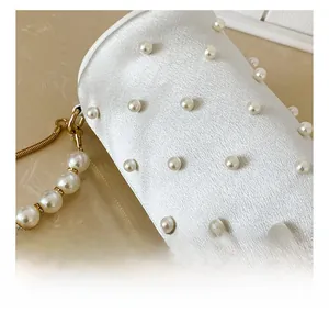 Detail of white satin handbag featuring faux pearl embellishments and gold chain