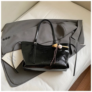Détail du sac cabas en cuir verni noir avec texture riche et pendentif de baseball