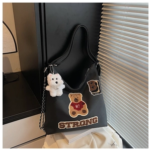 Dettaglio della borsa tote in pelle nera con patch orsetto e ciondolo a cane