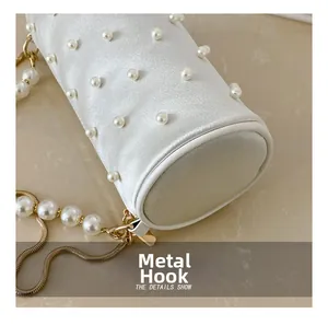 Detail of the golden hardware hook on a white satin pearl cylinder handbag