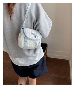 Back view of a model wearing a light blue bow-knot crossbody bag in a minimalist room