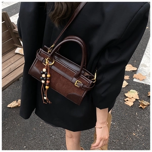 Dettaglio di una borsa a tracolla marrone con patchwork scamosciato e nappina con perline