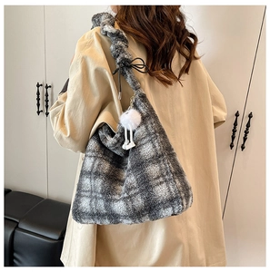 Detail of plush checkered tote bag featuring a white faux fur pompom and soft strap