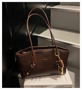 Detail of woven brown leather tote bag with gold logo and ethnic style bead charm