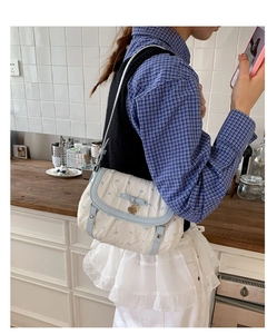 Detail of light blue quilted shoulder bag with bow floral print and gold heart charm