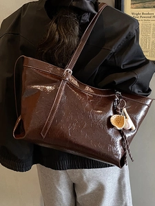 Grand sac fourre-tout en cuir verni marron avec pendentif baseball porté par un mannequin