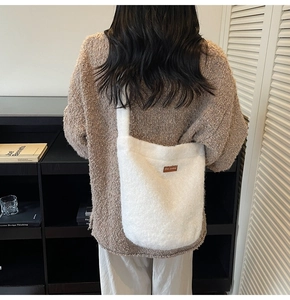 Detailopname van een pluche crèmekleurige bucket bag met logo patch en grote opslagcapaciteit