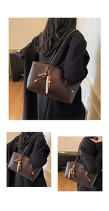 Detailed close-up of dark brown woven leather tote with gold logo and beaded charm detail