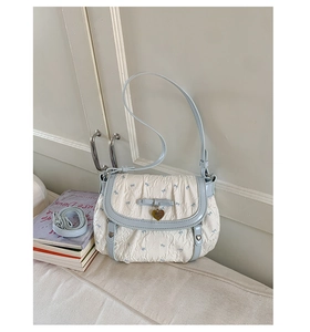 Detail of cream shoulder bag with blue trim, bow decoration, and heart-shaped pendant