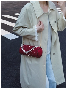 Detail view of red velvet cylinder bag with white pearls and gold chain strap in street style