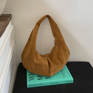 Détail macro du sac hobo en daim marron avec fermeture éclair posé sur des livres