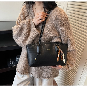 Detail of black woven texture tote bag with elegant beaded tassel and golden logo