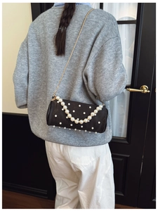 Detail of elegant black shoulder bag with pearl embellishments and gold chain strap