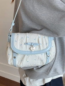 Quilted white shoulder bag with blue floral bows and heart-shaped metal tag worn by model
