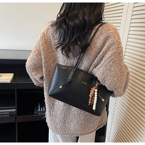 Detail of black woven tote bag featuring soft PU leather and vintage beaded charm accessory