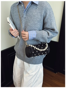 Fashionable black cylinder pearl handbag with gold chain strap worn by a stylish model