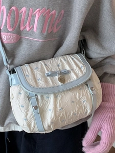 Cream crossbody bag with blue bow and floral pattern, styled as a shoulder bag