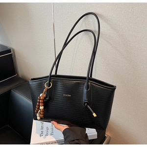 Detail of black woven leather tote bag with gold branding and beaded pendant accessory