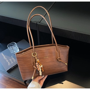 Detailed shot of brown woven tote bag with gold logo, long strap and beaded tassel charm