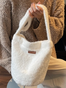 Pluche witte emmertas met bruin lederen label, getoond op een model voor de herfst