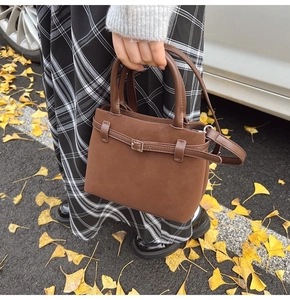 Detail of a dark brown suede tote bag with decorative straps on a golden ginkgo leaf background