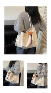 Detailed view of off-white tote bag with brown plush bear charm on a slim shoulder strap