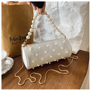 Close-up of white cylinder pearl handbag with gold chain strap on a wooden table