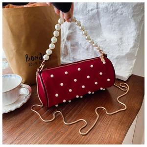 Detail view of burgundy velvet cylinder bag with pearls and golden chain strap