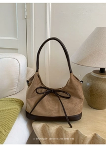 Detailed close-up of brown suede tote bag with leather straps and bow on wooden table