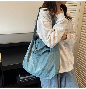 Close-up of a blue-green nylon tote bag featuring soft pleated texture and casual style