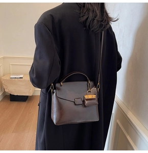Detail view of dark brown leather handbag with a mini bag charm worn by a model