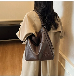 Detail of a dark brown leather tote bag with embossed logo worn by a woman in a trench coat