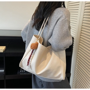 Macro shot of a cream leather tote bag featuring a cute brown plush bear charm and tassel