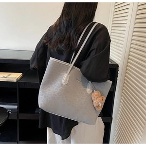 Detail of grey leopard embossed tote bag with plush bear charm on model shoulder