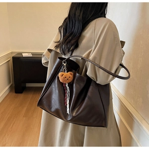 Detail of deep brown tote bag with soft faux leather texture and cute bear pendant