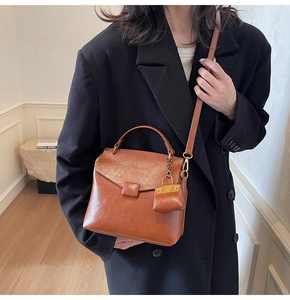 Detail of caramel leather crossbody bag with a mini side pouch charm and metal buckle