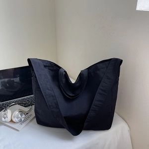 Close-up of a large black nylon tote bag with a laptop and headphones on a desk