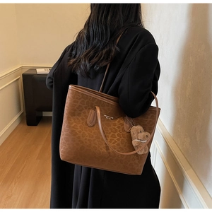 Detail of leopard print tote bag with plush bear charm and sleek shoulder strap